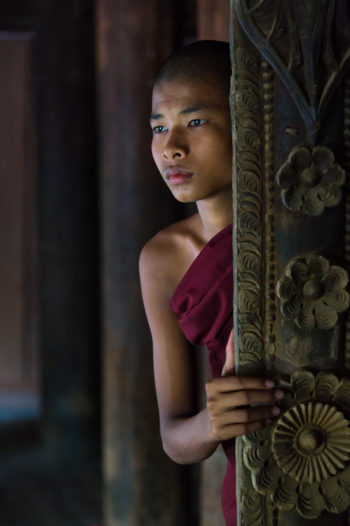 Young monk peeking through a window in the village of Shwe Kun Cha Hpaya close to Bagan in Myanmar.