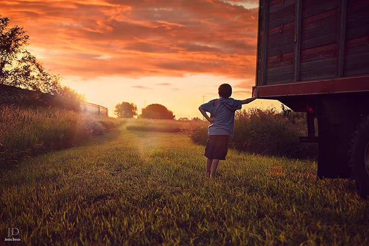 photo of a kid in the field next to a truck watching the sunset