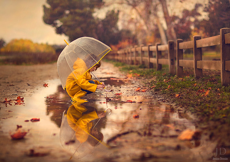 kid plays with a fallen leaf in a puddle after a rain storm.