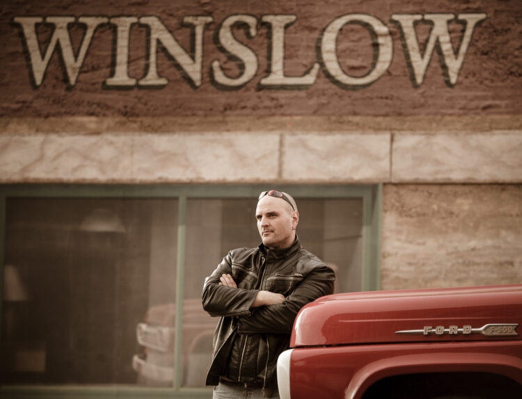Portrait photo of a man at standing on the corner park in Winslow Arizona showing how long camera lenses make good shots