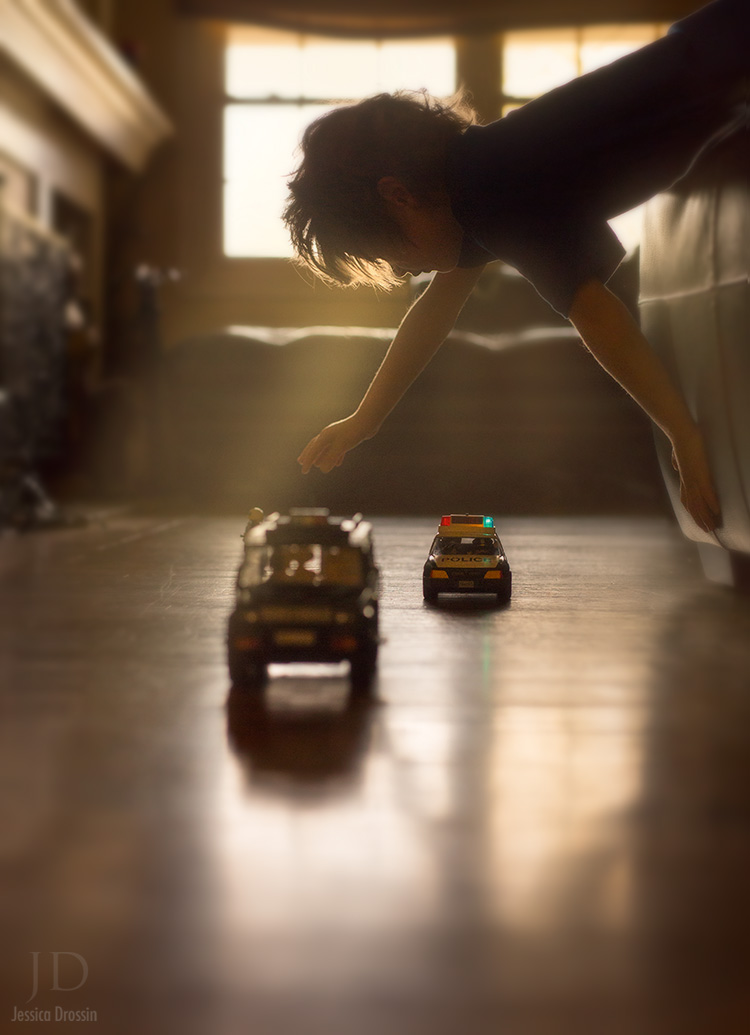 a young boy leans over the bed and plays with his toy cars on the floor
