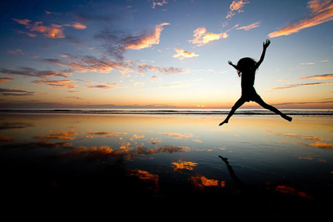 Photographers child in silhouette while jumping on the beach.