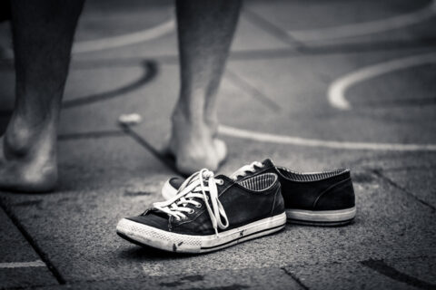a pair of shoes lie empty on the sidewalk next to the bare feet of the owner