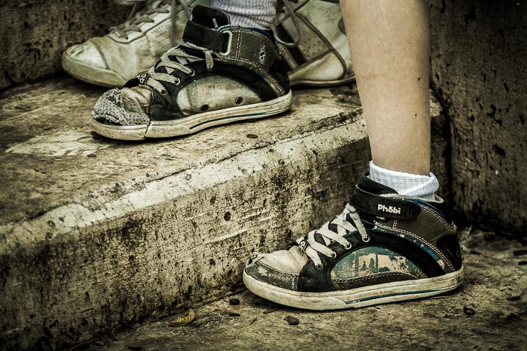 A childs foot in it's shoe with other shoes behind it